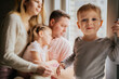 © Yulia Raneva - cute caucasian little boy standing on window sill. His parents and sister on background looking out the window. Home isolation during world pandemia. Image with selectie focus and toning