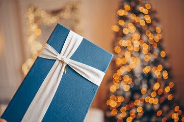 Blue present box against the background of a Christmas decorated tree in warm golden colors