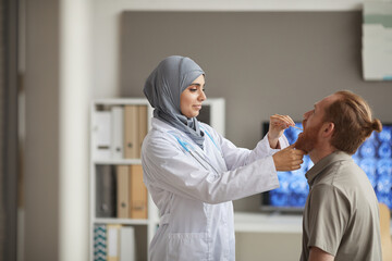 Wall Mural - Muslim female doctor in white coat examining the throat of the patient during medical exam at hospital