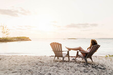 Woman Relaxing On Chair At Beach Against Sky During Sunset