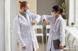 © AnnaStills - Two doctors in protective mask and in white coats greeting each other at the corridor of hospital