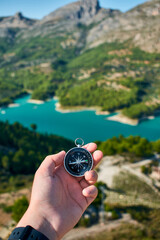 A man's hand holding a compass with a lake on background