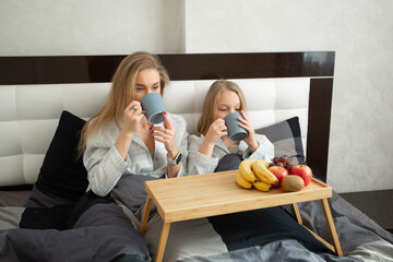 beautiful young mother with her daughter under the covers have breakfast in bed