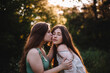© Cavan Images - Young woman kissing her girlfriend on the cheek in forest in summer