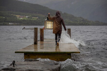A Person Carrying A Lantern On A Dock In The Rain