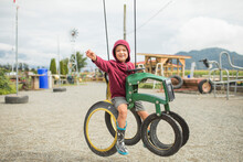 Young Boy Sits On Play Ride On Tractor At Farm Made From Recycled Tire