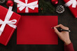 Hands writing red greeting card mockup with christmas decoration on grunge background.