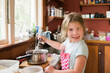 © Cavan Images - Young girl smiling and mixing hot baking mixture in messy kitchen