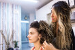© Cavan Images - Hairdresser combing client with long curly hair against wall mirror at Hair Salon