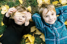 Happy Siblings Lying On The Ground With Yellow Leaves Around Them