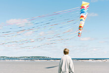 A Boy Admiring A Large Kite Flying Past Him On A New England Beach