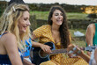 © Cavan Images - Smiling woman playing guitar having fun with group of friends