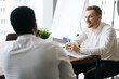 © dikushin - Smiling businessman listening to African American business partner talking about new project sitting at the desk in modern conference office room. back view.