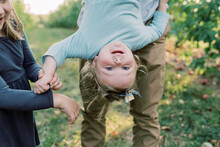 A Cute Toddler Girl Being Held Upside Down With Her Sister Cheering