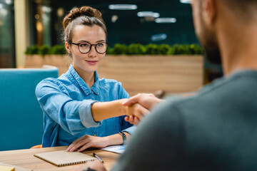 Two 25s business partners shaking hands at office desk