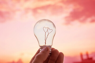 Man hold light bulb in hand, inside which there are two hearts against the sky and the sun. Innovation, brainstorming, solution concepts. New idea