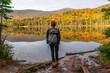 © Cavan Images - Young woman staring out at colorful trees reflecting in lake water.