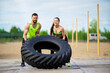 © Georgii - Crossfit couple exercising with tire outside, powerful sports pair guy and girl lifting weight