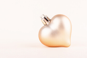 Wall Mural - Christmas tree toy in the shape of a heart golden color on a light background with copy space. Close up.