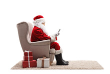 Profile Shot Of Santa Claus Sitting In An Armchair And Using A Mobile Phone