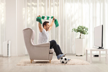 Young man cheering with a scarf and watching a football game on tv