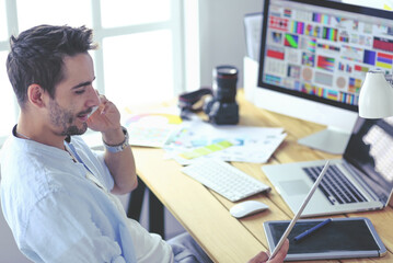 Poster - Portrait of young designer sitting at graphic studio in front of laptop and computer while working online.