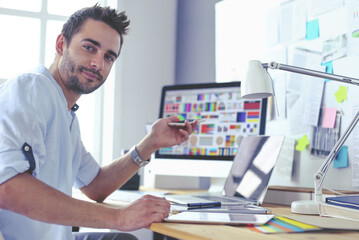 Poster - Portrait of young designer sitting at graphic studio in front of laptop and computer while working online.