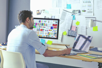 Poster - Portrait of young designer sitting at graphic studio in front of laptop and computer while working online.