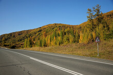 A Road Sign On The Side Of A Straight Paved Two-lane Road Going Through An Autumn Valley.