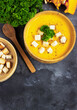 Pumpkin soup with cream, bread and fresh parsley in a rustic metal plate over grunge black background. Top view, copy space