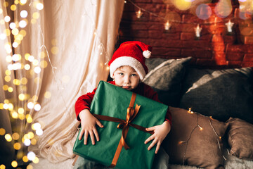 Wall Mural - A boy holding a large box in a green package and a bow with a gift. Christmas mood