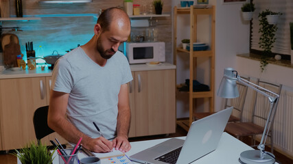 Poster - Businessman writing notes while working late on computer in home kitchen. Busy focused employee using modern technology network wireless doing overtime for job reading typing, searching