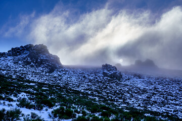 Wall Mural - Paisaje nevado en la montaña de La Morcuera Madrid con nieve, nubes, niebla y frío intenso. Sol saliendo entre las nuebes en el horizonte.