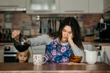 Tired Mother, Trying To Pour Coffee In The Morning. Woman Lying On Kitchen Table After Sleepless Night