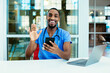 © Carlos David - Portrait of a smiling male doctor wearing blue scrubs uniform waving at camera, talk to patient online on phone