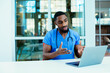 © Carlos David - Portrait of a male doctor wearing blue scrubs uniform using laptop to talk to patient online