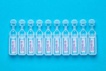 Coronavirus treatment concept. Close-up of ten ampoules with vaccine COVID-19 flat layed on a blue background. Global pandemic outbreak and healing the deadly coronavirus. Macro photograph.