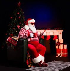 Wall Mural - Photo of santa sit chair hold mug telephone look screen wear x-mas suspenders cap isolated decorated background