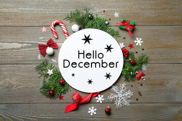 Greeting card with text Hello December, fir tree branches and Christmas decor on wooden background, flat lay