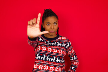Wall Mural - Young beautiful African American woman standing against red background making fun of people with fingers on forehead doing loser gesture mocking and insulting.