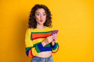 Poster - Photo of charming pretty brunette hair young lady blow kiss hold telephone wear pullover isolated on bright yellow background