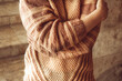 Female hugging herself with arms. Young woman in a cozy beige sweater spends time outdoors. Lifestyle portrait of female