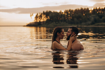 Romantic photo session in the water. A guy and a girl swim in the lake in the evening. Beautiful sunset.