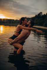 Romantic photo session in the water. A guy and a girl swim in the lake in the evening. Beautiful sunset.