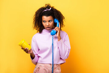 shocked african american woman talking on blue retro telephone and holding eco cup on yellow