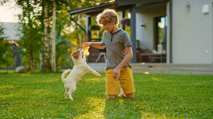 Cute Boy Plays with His Favourite Dog Friend while Having Picnic Outdoors on the Lawn. He Pets and Teases His Little Smooth Fox Terrier with His Favourite Toy. Idyllic Summer House.