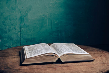 Beautiful open Holy Bible on a old brown oak wooden table.  Green wall background.