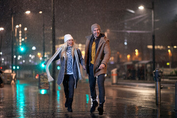 Wall Mural - A young cheerful couple excited about walk on a snowy weather in the city. Love, together, walk, snow, city