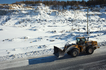 Wall Mural - Wheeled front-end loader moves along the road in a snow-covered stone quarry, close-up.