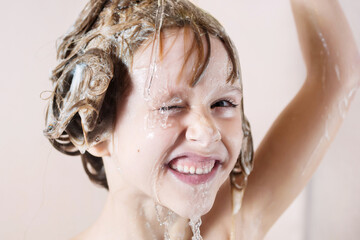 Wall Mural - a little girl washes her hair with shampoo. water pours on her head and she closes her eyes and laug